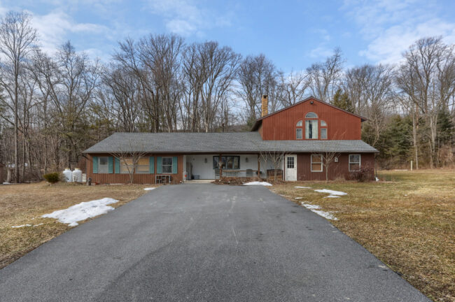 Front exterior of country home for sale at 133 Fort Henry Road in Bethel Pennsylvania with long driveway and wooded setting